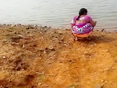 Indian woman peeing in the filth by a lake